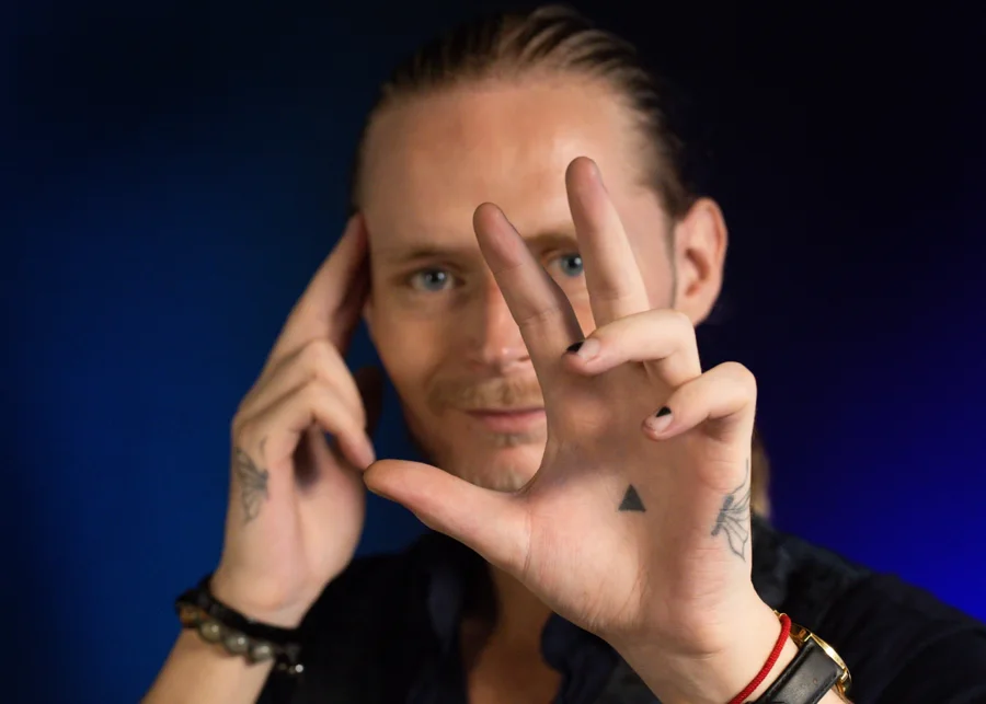 Jesper K. Lassen holding up an open hand, a small triangle drawn on his palm, against a dark blue background